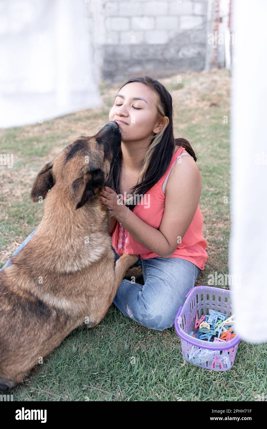 Una giovane donna ispanica sta baciando il suo cane in giardino mentre fa il bucato Foto Stock