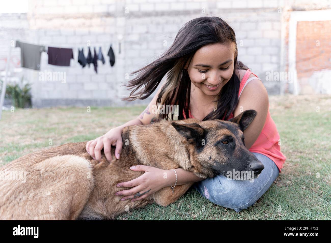 Una giovane donna ispanica sta abbracciando il suo cane in giardino mentre fa il bucato Foto Stock