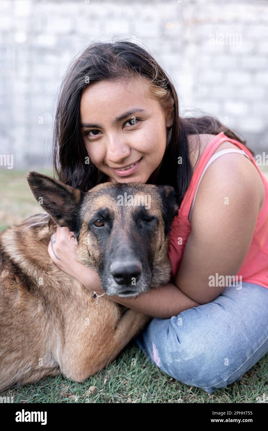 Ritratto di una giovane donna ispanica che abbraccia il suo cane con un occhio in giardino Foto Stock