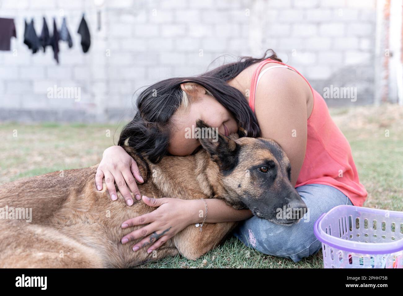 Una giovane donna ispanica sta abbracciando il suo cane in giardino mentre fa il bucato Foto Stock