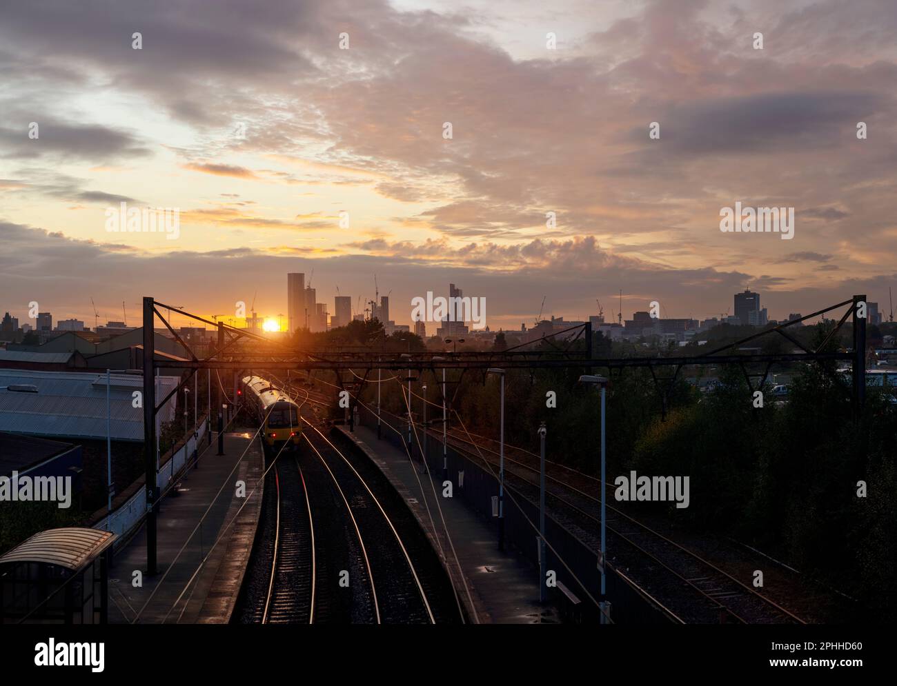 La stazione ferroviaria Sunset Ashburys si trova a Manchester, la linea ferroviaria Manchester-Glossop con lo skyline della città e le nuove torri della città Foto Stock