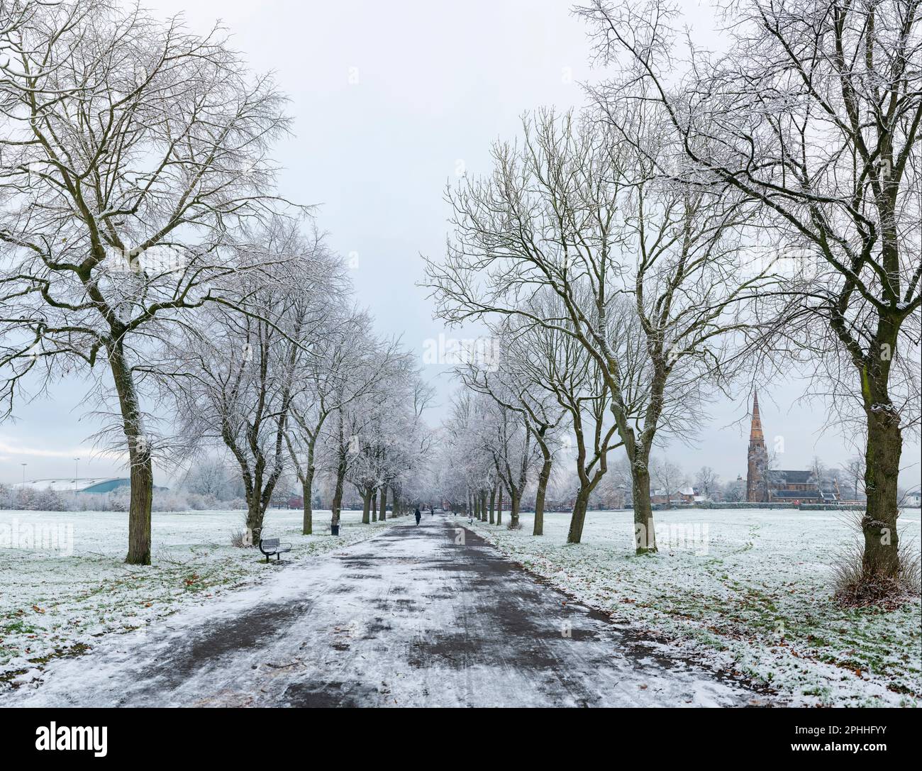 Avenue of Trees in Platt Fields Park nel sud di Manchester su un inverno innevato e gelido mattina, con la chiesa di Holy Trinity Platt in lontananza. Foto Stock