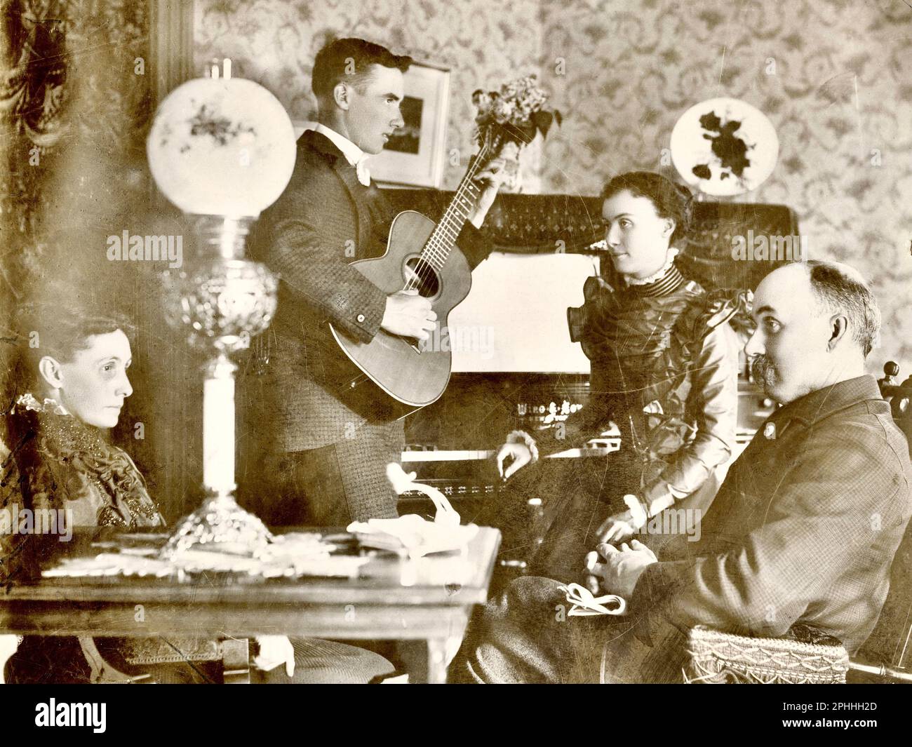 Casa vittoriana interno circa 1900, uomo che gioca chitarra a famiglia in salotto Foto Stock