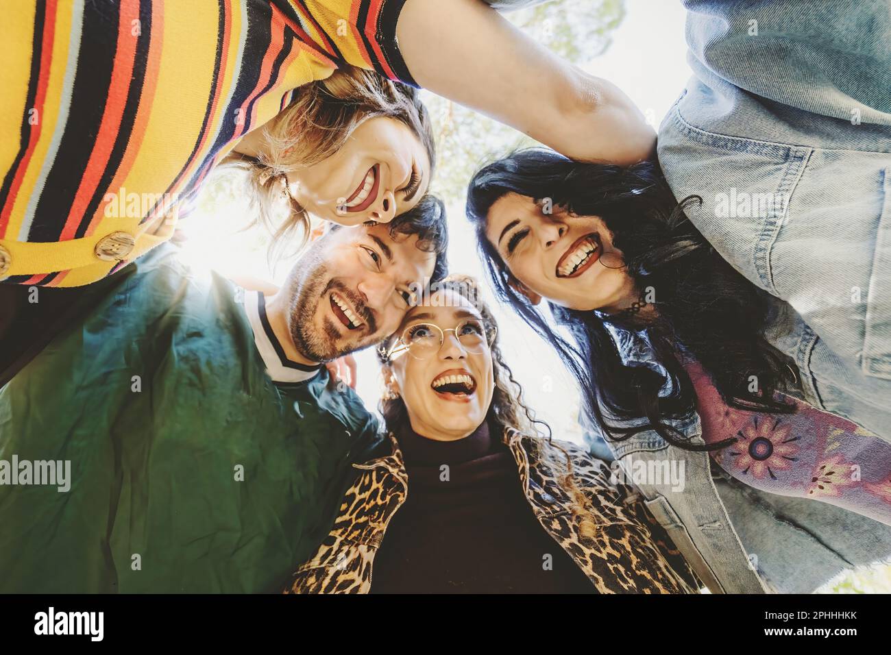 Quattro amici in 90s abiti casual abbracciando in cerchio in un parco pubblico, godendosi, sorridendo e ridendo. Foto Stock