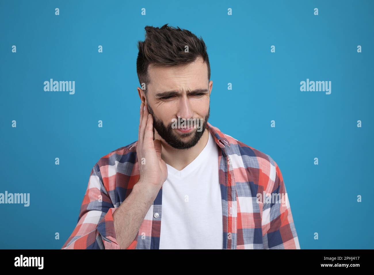 Uomo che soffre di dolore all'orecchio su sfondo azzurro Foto Stock