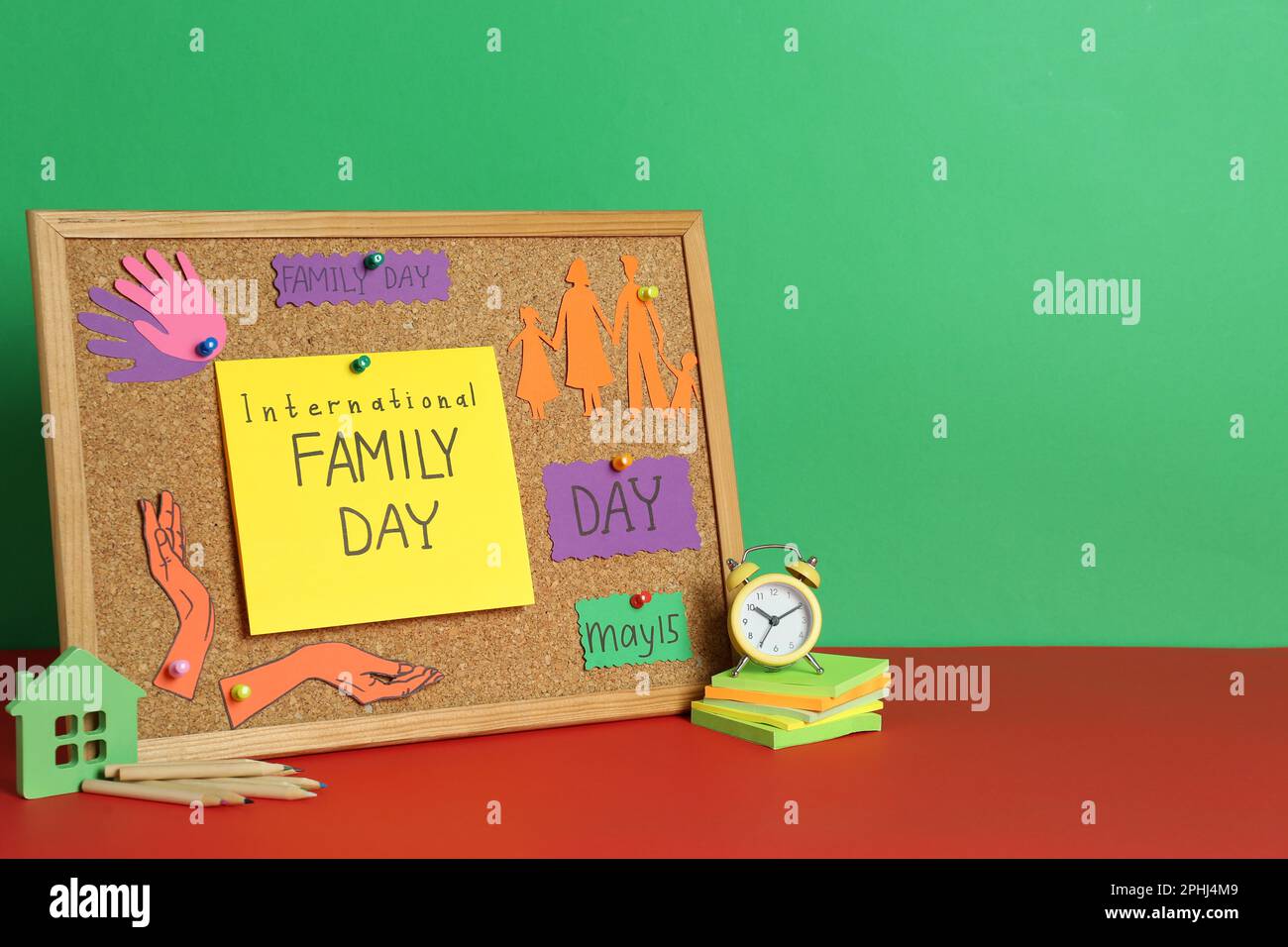 Felice Giornata Internazionale della Famiglia. Composizione con cartellone, cartoncini e cancelleria su tavolo rosso su sfondo verde, spazio per il testo Foto Stock
