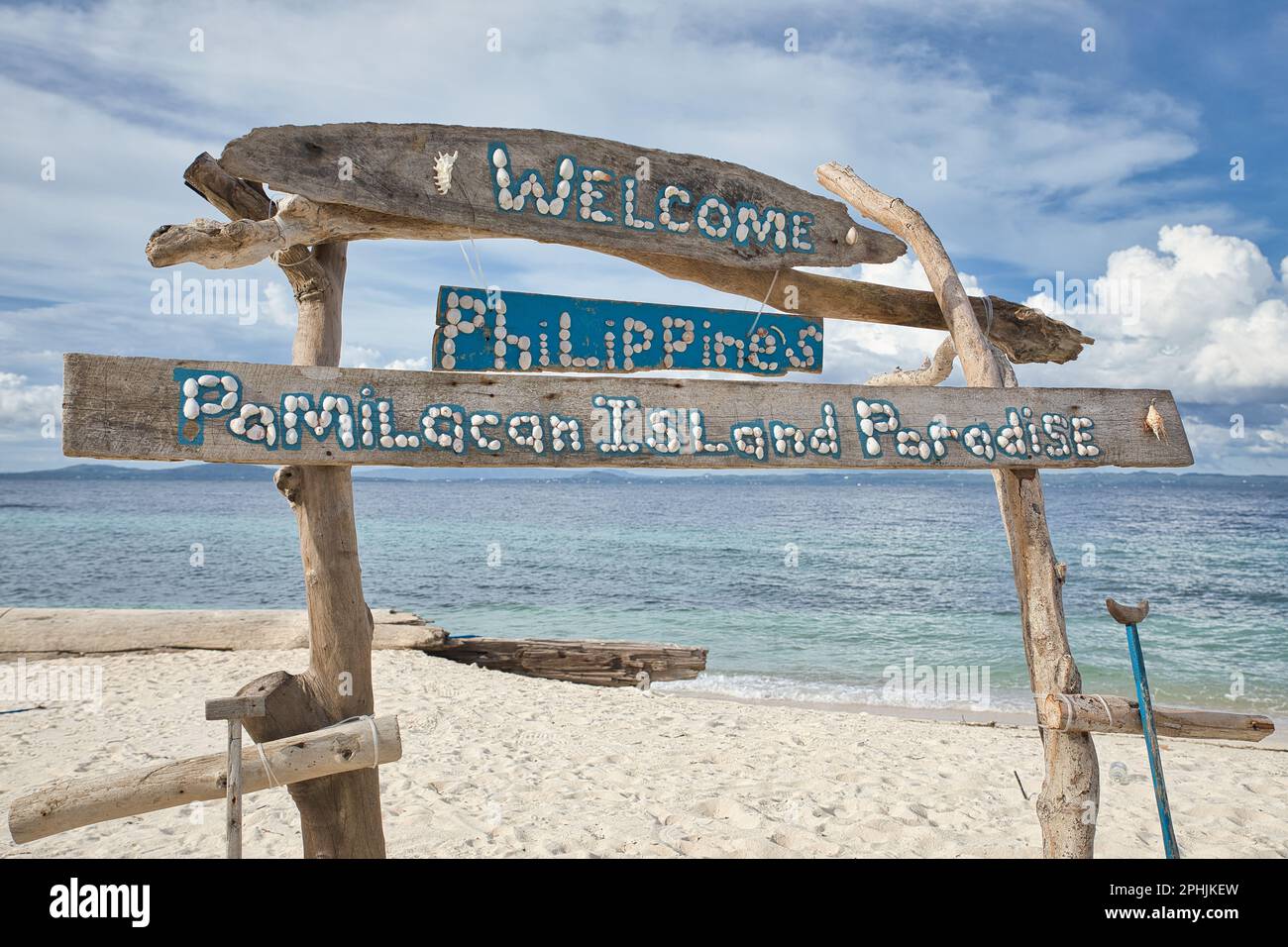 Idilliaca spiaggia di sabbia bianca di Pamilacan Island nelle Filippine con un cartello di benvenuto in legno in primo piano. Foto Stock