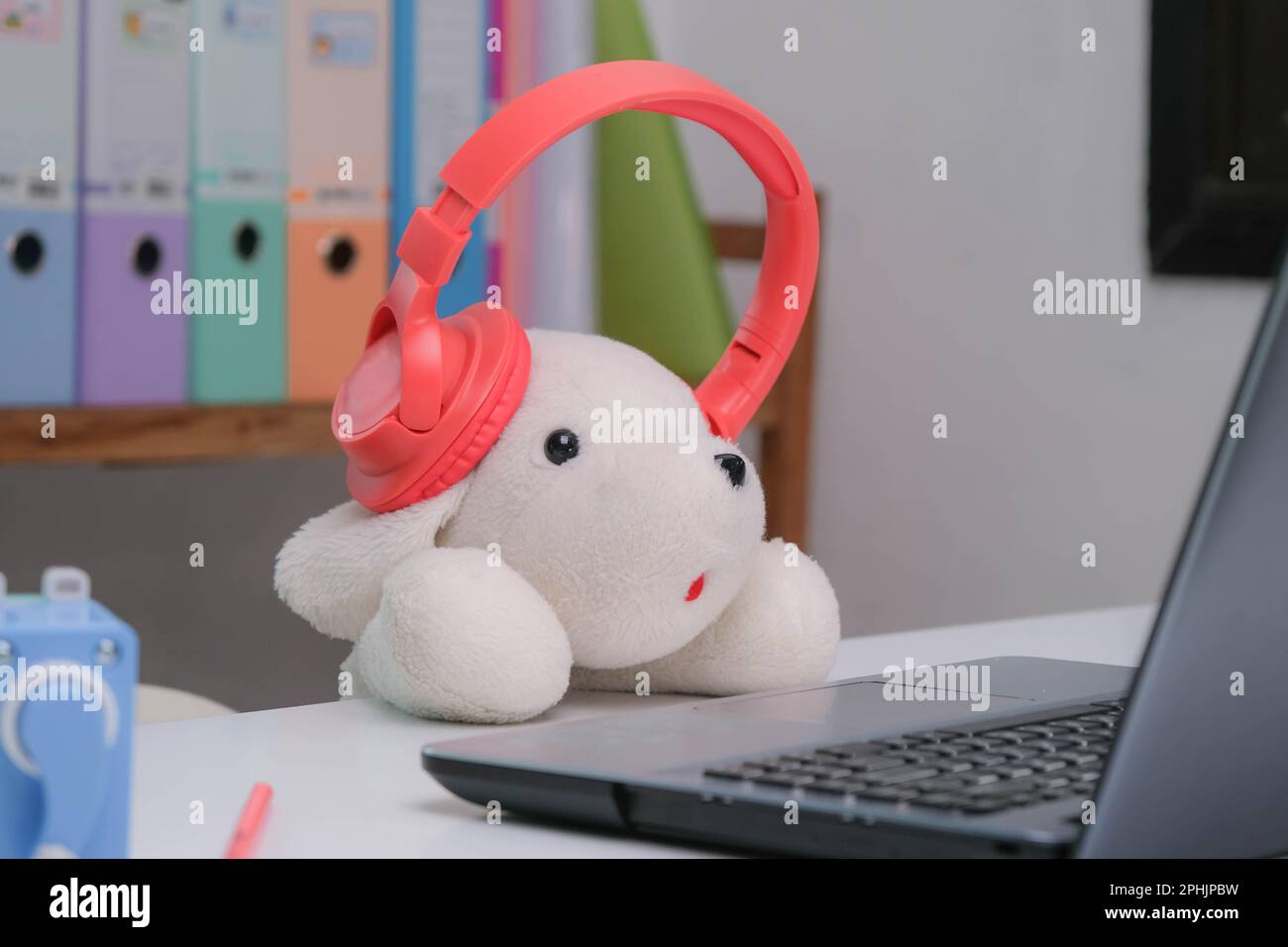 Cane giocattolo bianco imbottito indossare cuffie e guardare il computer portatile. Soffice bambola bianca con cuffie. Foto Stock