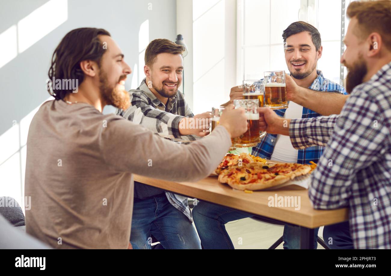 Sorridendo i migliori amici uomini con birra e pizza che si divertivano seduti a casa. Foto Stock