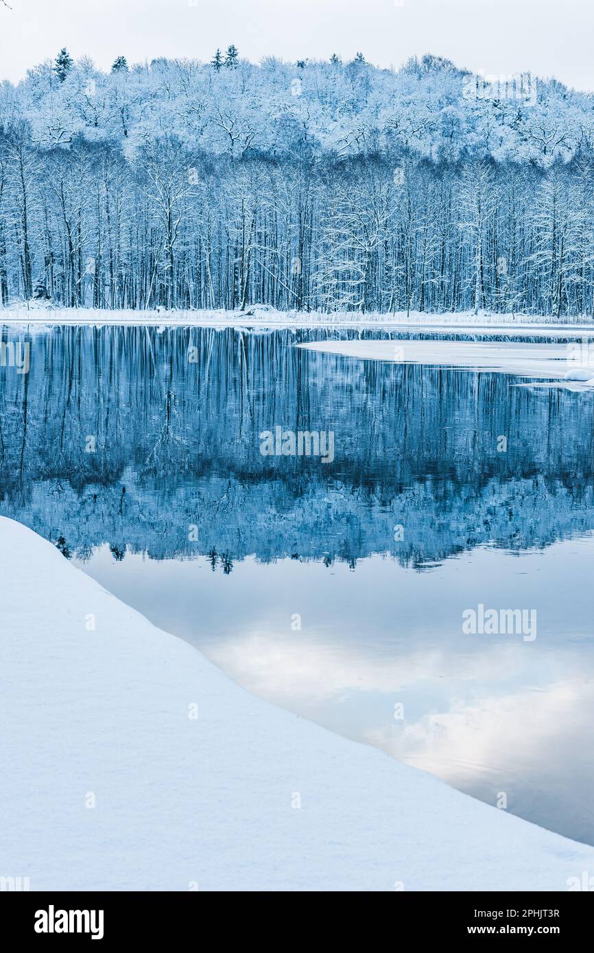 Una tranquilla scena invernale in Svezia, con ghiaccio gelido e neve che si riflettono sulla superficie dei fiumi - un perfetto esempio di bellezza naturale. Foto Stock