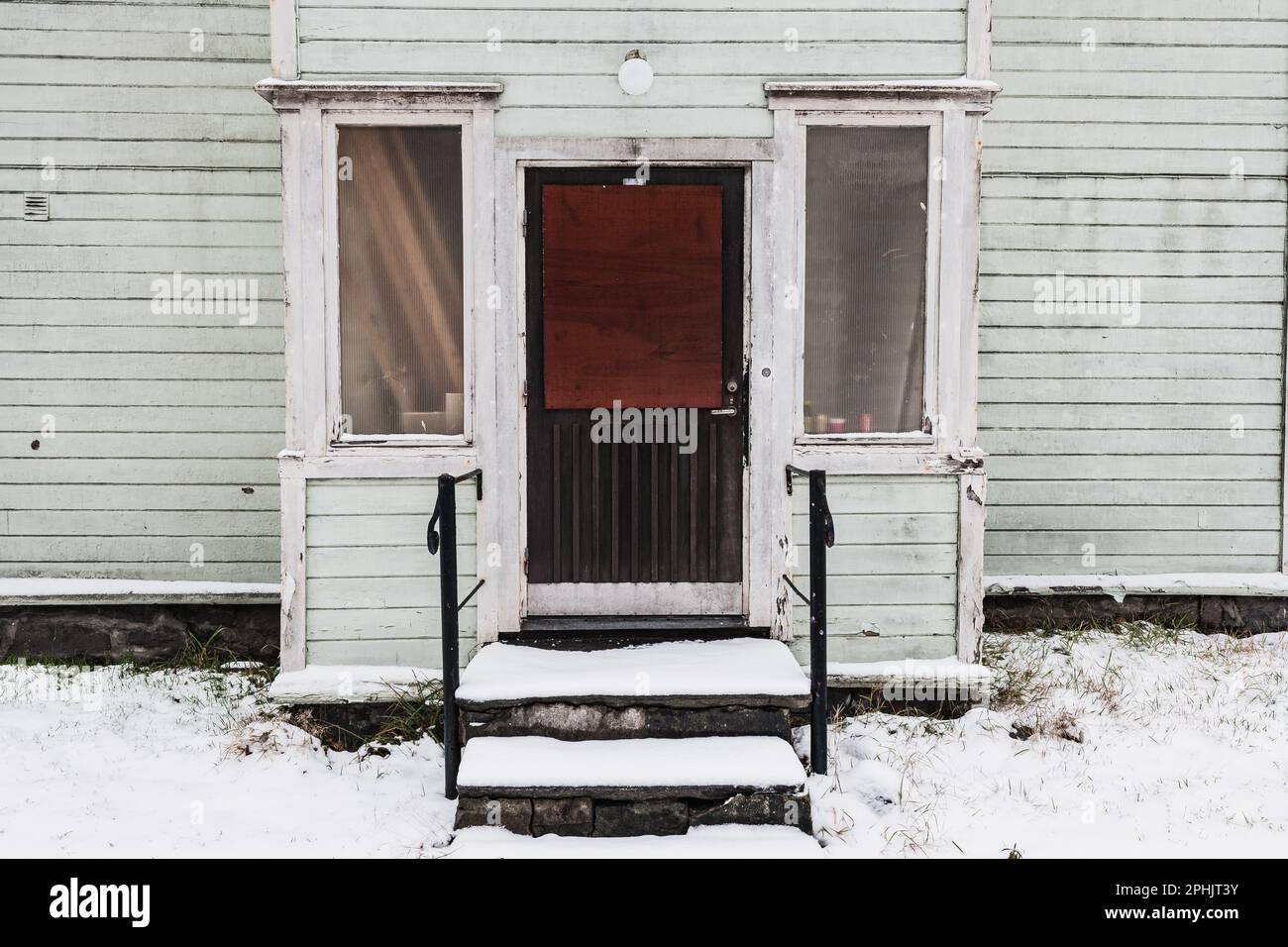 Una casa usurata e abbandonata con neve bianca e una porta d'ingresso chiusa sul suo esterno. Nessuna gente intorno nel giorno. Foto Stock