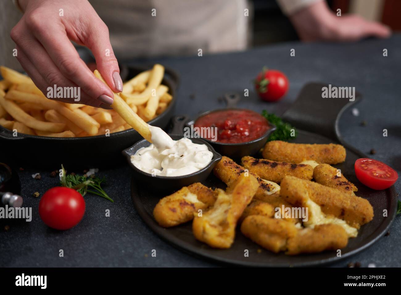 Donna immerge le patatine fritte in salsa di tuffo con mozzarella di formaggio fritta bastoni su un tavolo Foto Stock