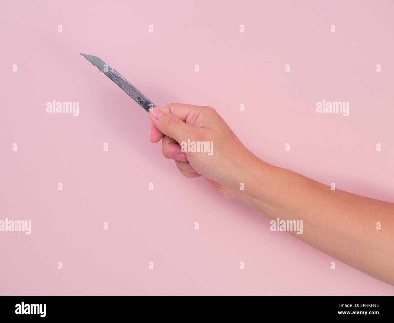 Primo piano della lama femmina per tenere la mano isolata su sfondo rosa. Mano che tiene una taglierina d'argento con una lama affilata in primo piano. Foto Stock