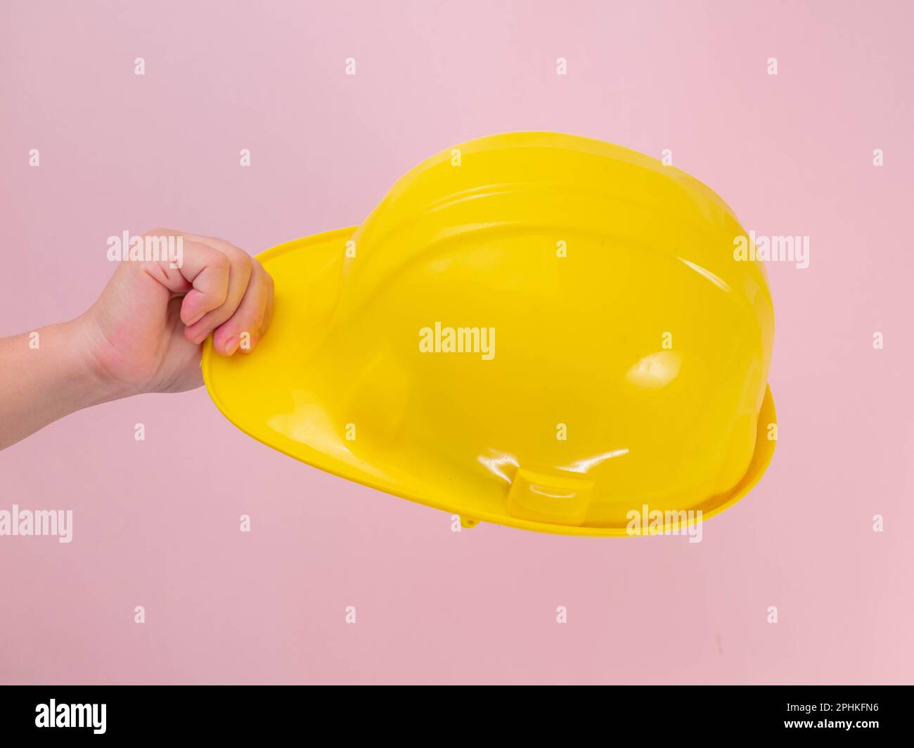 Primo piano della mano di un ingegnere femminile che tiene il casco di sicurezza giallo su sfondo rosa. Mano umana che tiene un elmetto. Foto Stock