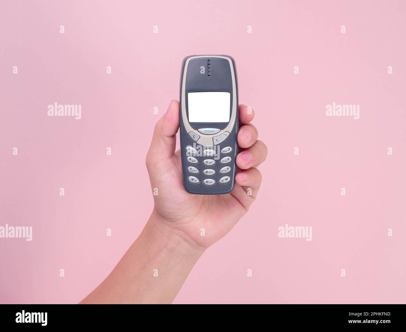 Primo piano mano che tiene il telefono cellulare Nokia 3310 isolato su sfondo rosa. Mano femmina che tiene vecchio telefono usato Nokia 3310. Foto Stock