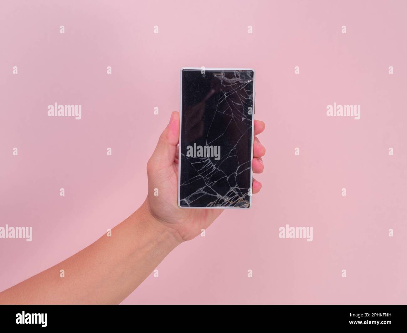Primo piano della mano che tiene il telefono cellulare con touch screen rotto su sfondo rosa. Mano femmina che tiene il vecchio telefono con schermo incrinato e danneggiato. Foto Stock