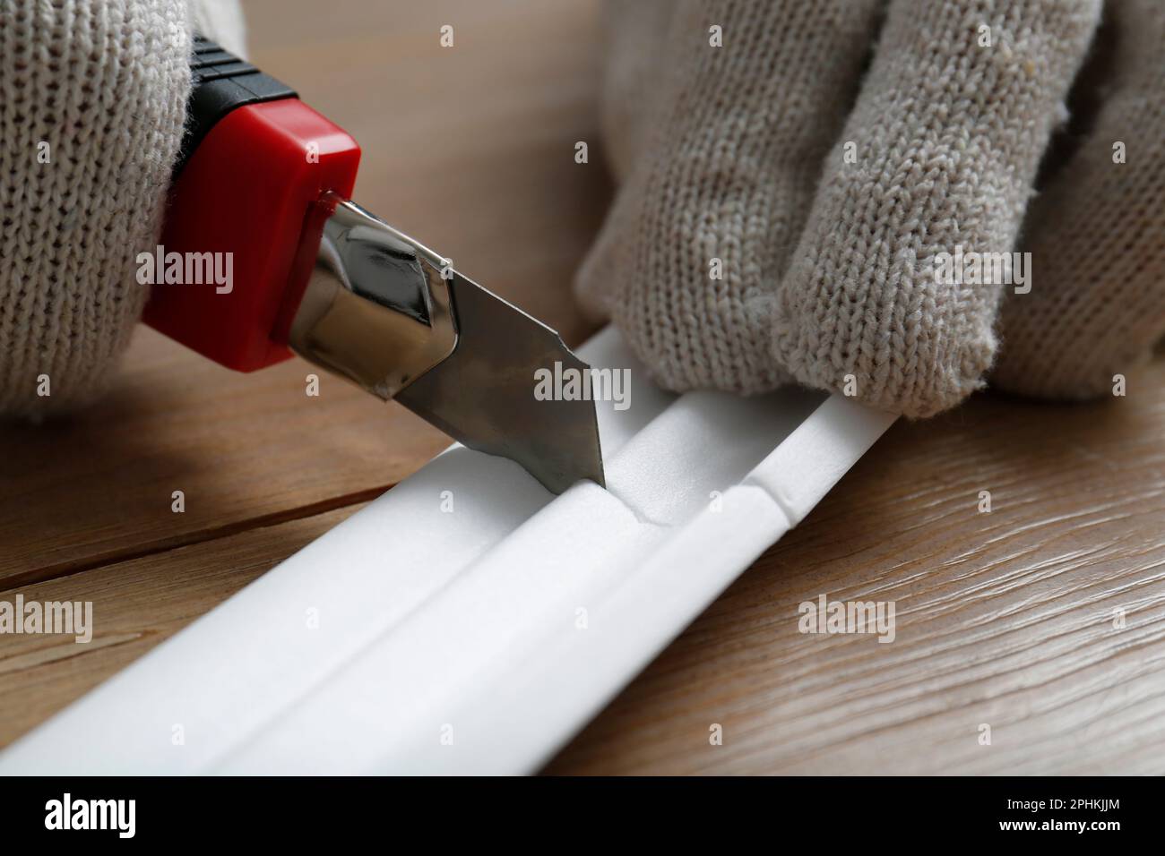 Lavoratore che taglia lo stampaggio della corona in schiuma con un coltello di servizio al tavolo di legno, primo piano Foto Stock