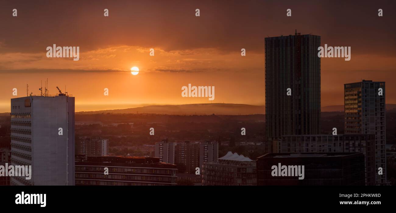 Un tramonto rosso e arancione, caldo e luminoso dal centro della città. Si affaccia sulle torri di Manchester fino alle colline lontane dall'alto. Foto Stock