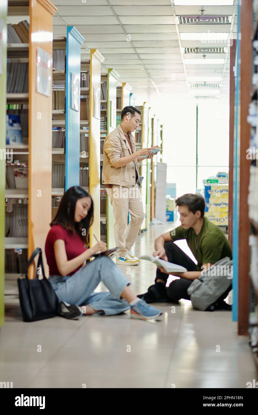 Gruppo di studenti seduti al piano della biblioteca Foto Stock