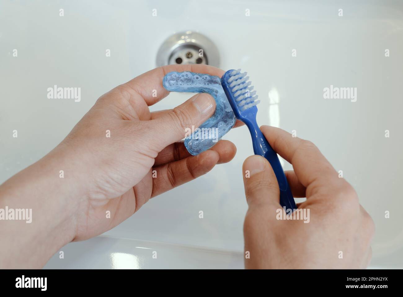 primo piano di un uomo che pulisce la sua stecca occlusale blu usando uno spazzolino da denti in un lavandino del bagno Foto Stock