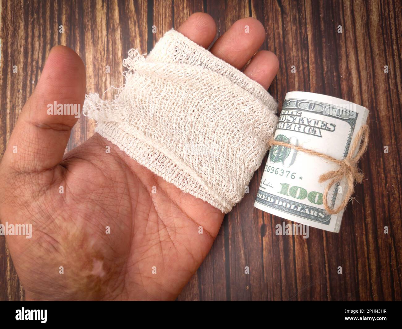 Bendaggio a mano e banconote su sfondo di legno. Concetto di assicurazione medica. Foto Stock