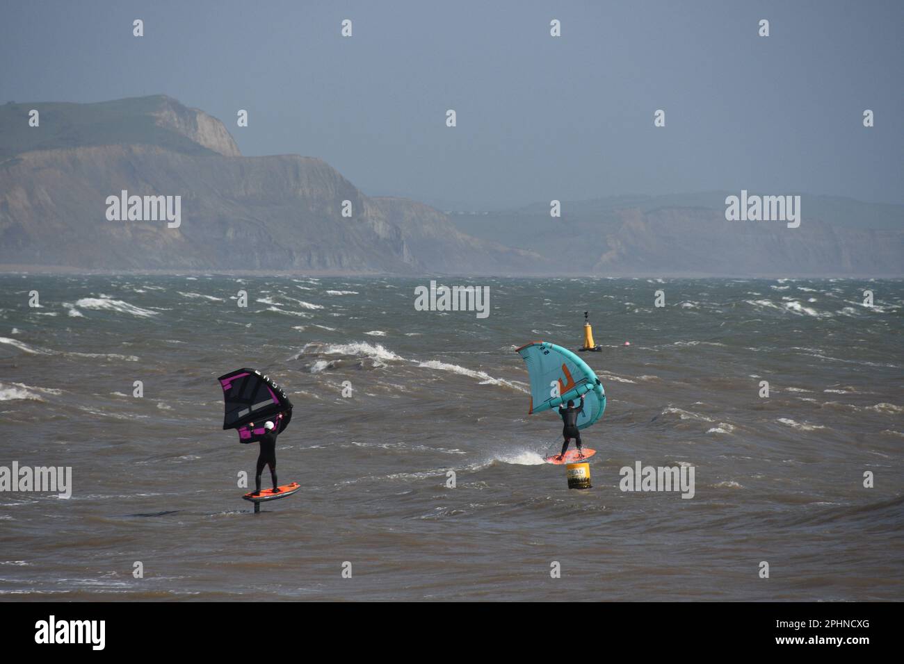 Un paio di Wing Foil Surfers scivola attraverso un mare mosso alimentato da una brezza rigida al largo della costa Jurrasic a Lyme Bay. Dorset.UK Foto Stock
