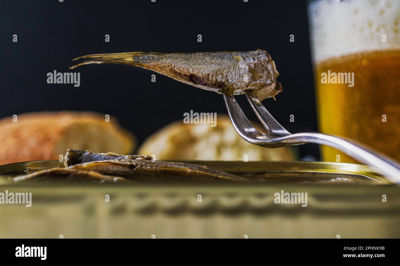Sardina in scatola su una forchetta piccola. Bicchiere di birra sullo sfondo. Foto Stock