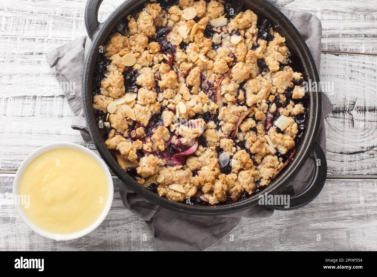 Torta Smulpaj Svedese crumble con mele e mirtilli serviti con salsa alla vaniglia fatta in casa closeup sul tavolo di legno. Vista orizzontale dall'alto Foto Stock