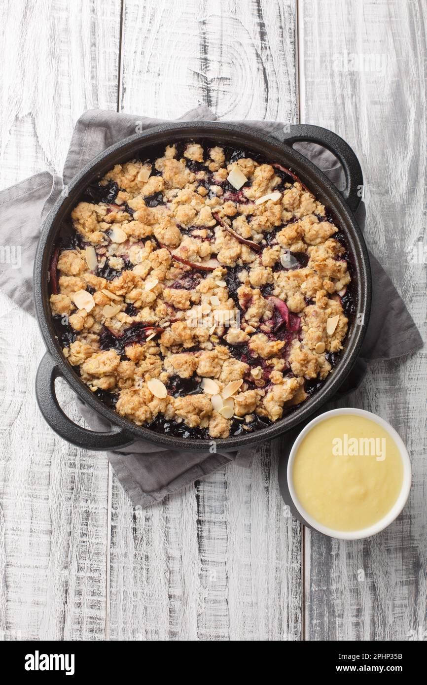 Crumble di frutta svedese Pie Smulpaj con salsa alla vaniglia fatta in casa closeup sul tavolo di legno. Vista verticale dall'alto Foto Stock