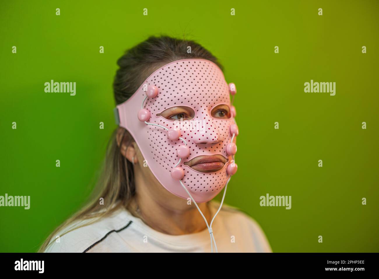 Vista ravvicinata della donna con maschera massaggiatore facciale rosa su sfondo verde. Svezia. Foto Stock
