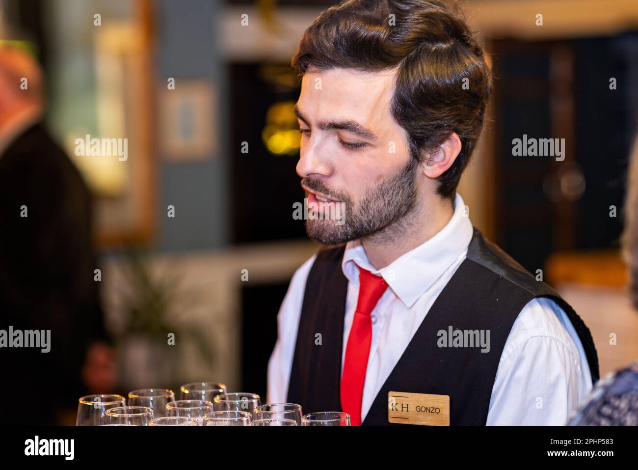 Primo piano del giovane e bel cameriere maschile che serve un vassoio di bicchieri da champagne alla festa del Knoll House Hotel, Studland, Dorset, Regno Unito, il 14 marzo 2023 Foto Stock