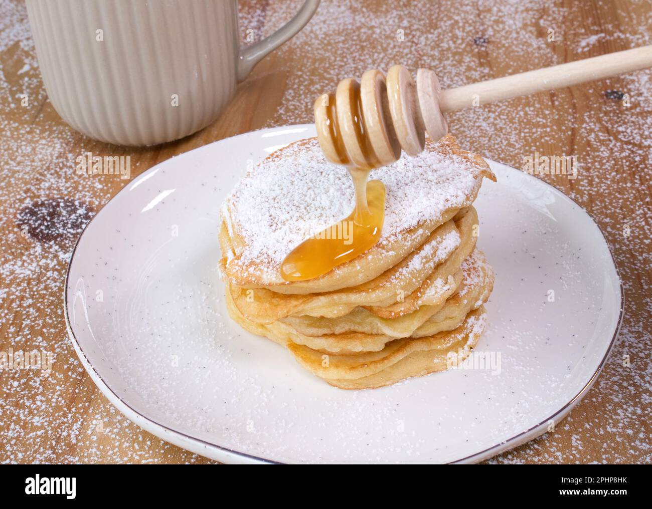 Pila di frittelle fatte in casa su un piatto bianco con una tazza di caffè e miele su un tavolo di legno, ID immagine: 2PHP8HK Foto Stock
