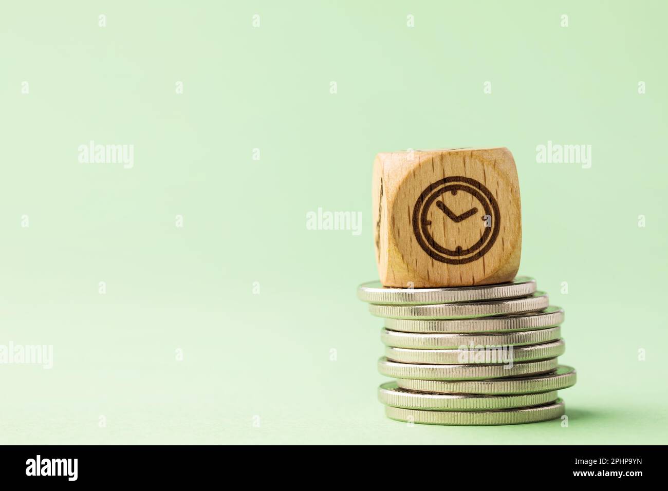 Cubo di legno su una pila di monete con spazio di copia su uno sfondo verde, un concetto sul tema del tempo è denaro Foto Stock