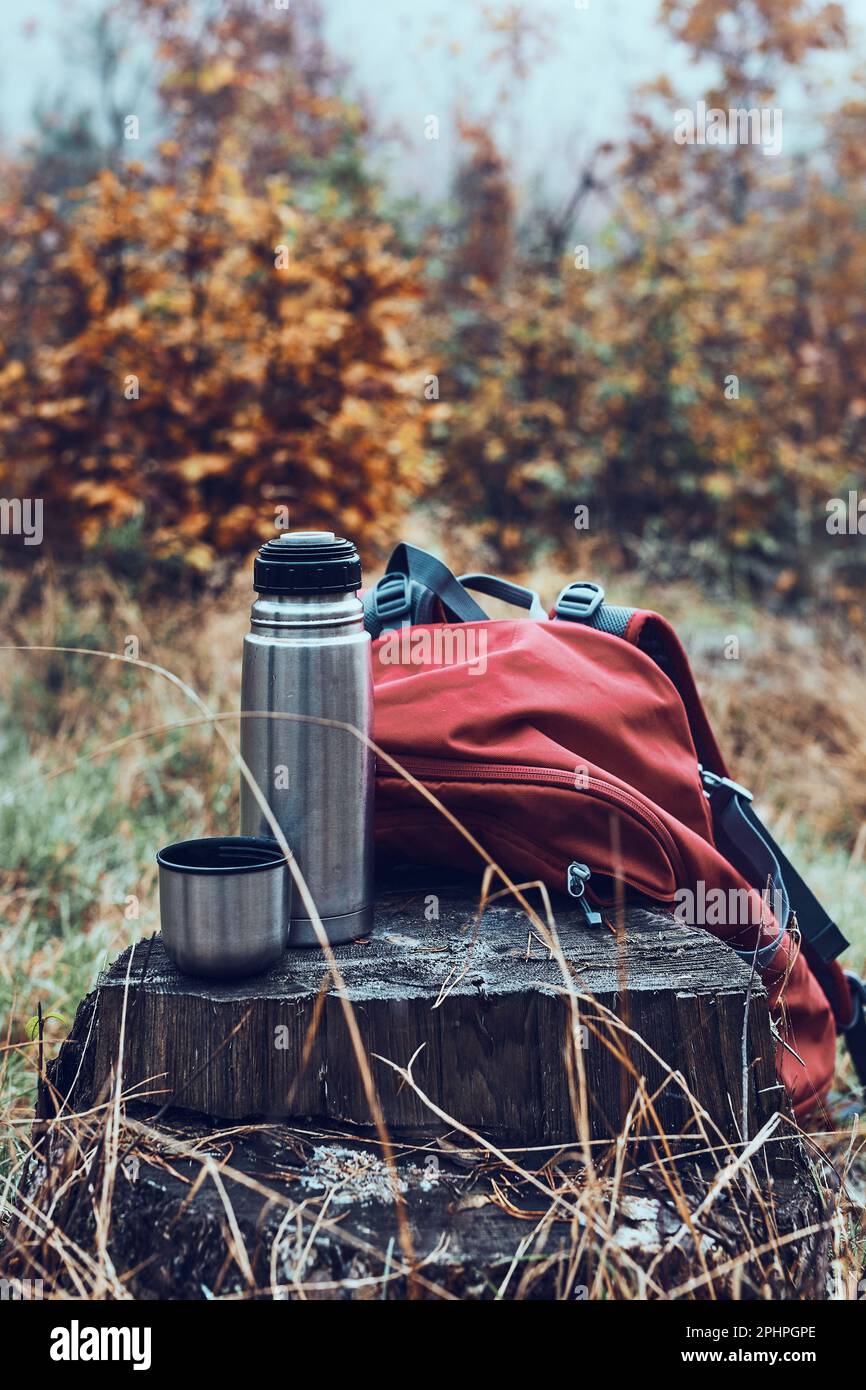 Chiudi la beuta thermos e lo zaino messo dal tronco dell'albero durante la pausa durante il viaggio autunnale nelle giornate fredde autunnali Foto Stock