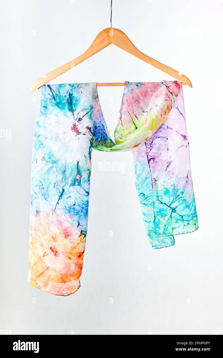 Sciarpa legata dipinta a mano e colorata di seta appesa su un appendiabiti su sfondo grigio. Donna moda, legando una sciarpa, indossando una sciarpa. Modi eleganti per legare e w Foto Stock