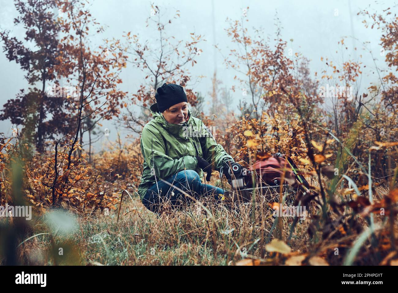 Donna con zaino in pausa durante il viaggio autunnale bere una bevanda calda da thermos beuta il giorno freddo autunnale. Attiva donna di mezza età che vagare arou Foto Stock