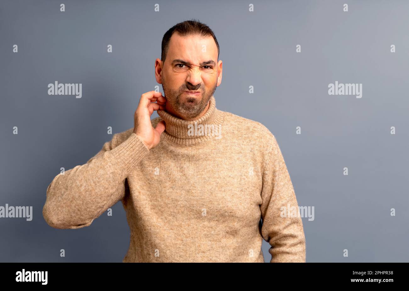 Uomo bearded di mezza età graffiandosi si è evidenziato con collare rosso su sfondo grigio studio, copia spazio. L'uomo turbato che soffre di prurito, eruzione cutanea sopra Foto Stock