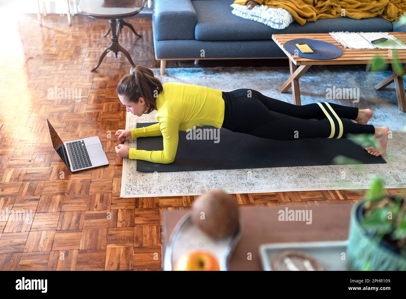Donna che fa l'asse sul pavimento nel paese e che guarda l'addestramento in linea sul Internet usando il laptop. Foto Stock