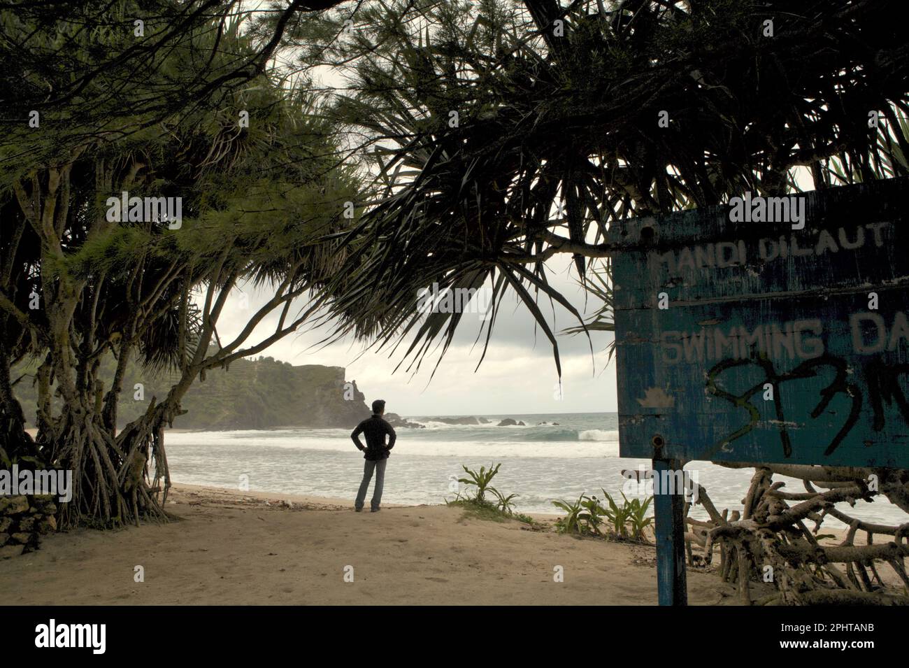 Dadang Sukandar, un arrampicatore della roccia, gode il paesaggio mentre sta levandosi in piedi sulla spiaggia sabbiosa all'arrivo, che domina una collina calcarea e l'Oceano Indiano in un'area costiera chiamata spiaggia di Siung, che è amministrativamente situato a Duwet, Purwodadi, Tepus, Gunungkidul, Yogyakarta, Indonesia. La spiaggia e' una delle popolari destinazioni ricreative costiere di fronte all'Oceano Indiano nella speciale regione di Yogyakarta. Per gli appassionati di arrampicata su roccia, Siung Beach offre più di 200 percorsi sportivi che sono già stabiliti sulla faccia delle sue colline calcaree. Foto Stock