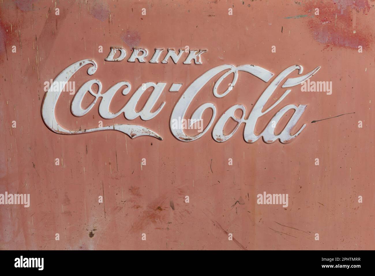 Primo piano del frigorifero con le parole: BERE COCA-COLA in lettere bianche. Lato rosso sbiadito con striature, ruggine e un look vintage molto resistente alle intemperie. Foto Stock