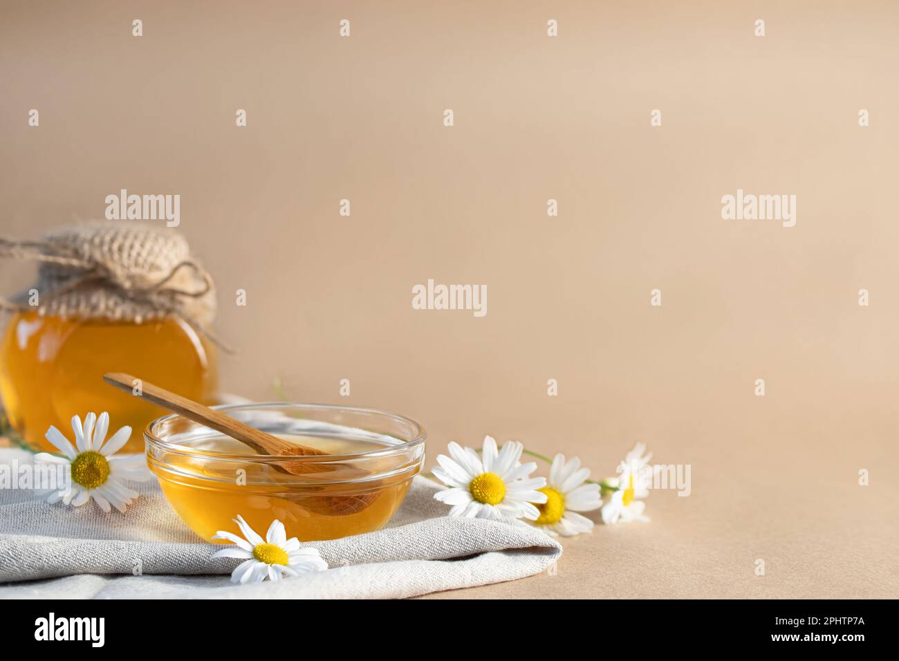 Sciroppo di camomilla in una piccola ciotola e in un vasetto e fiori di camomilla su un asciugamano da cucina di lino, spazio copia. Foto Stock