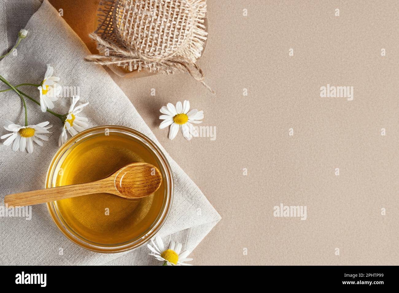 Sciroppo di camomilla in una piccola ciotola e in un vasetto e fiori di camomilla su un asciugamano da cucina di lino, spazio copia. Foto Stock