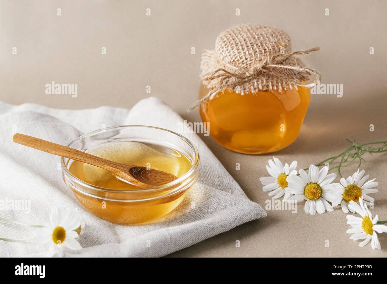 Sciroppo di camomilla in una piccola ciotola e in un vasetto e fiori di camomilla su un asciugamano da cucina di lino. Foto Stock
