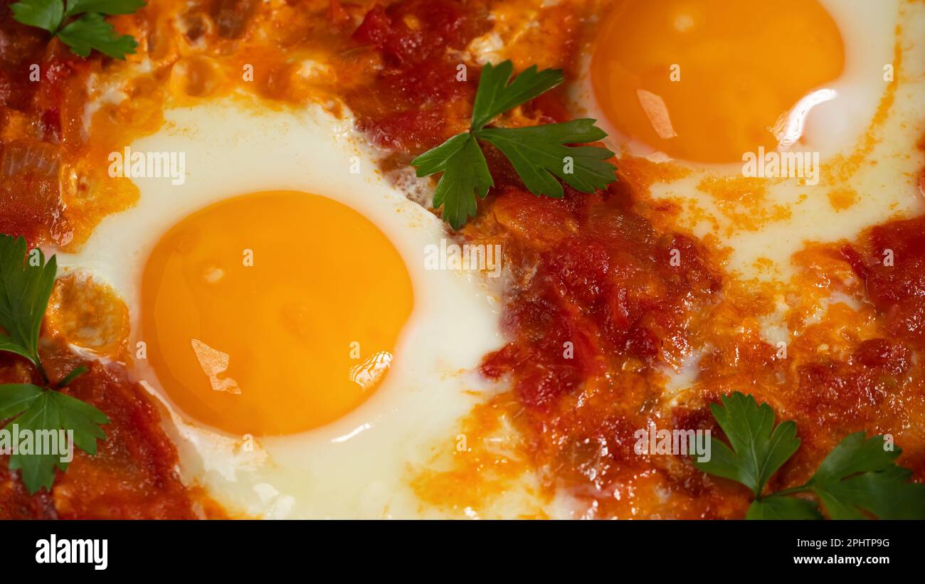 Due uova shakshuka in salsa di pomodoro con pomodori freschi, spezie ed erbe aromatiche. Uova strapazzate per primo piano. Foto Stock