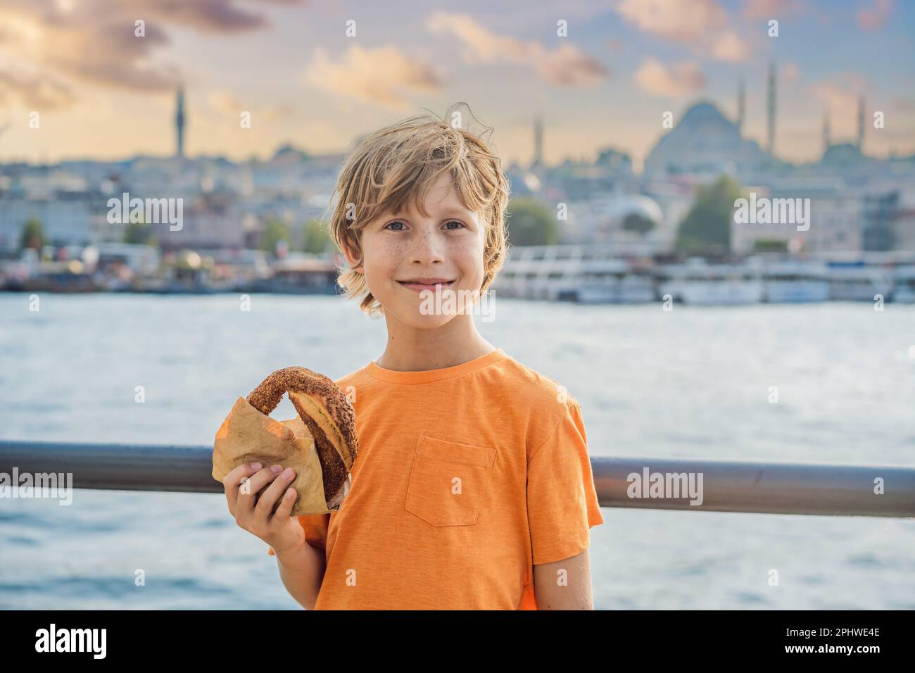 Ragazzo a Istanbul che faceva colazione con Simit e un bicchiere di tè turco. Bicchiere di tè turco e bagel Simit contro la baia del corno d'oro a Istanbul Foto Stock