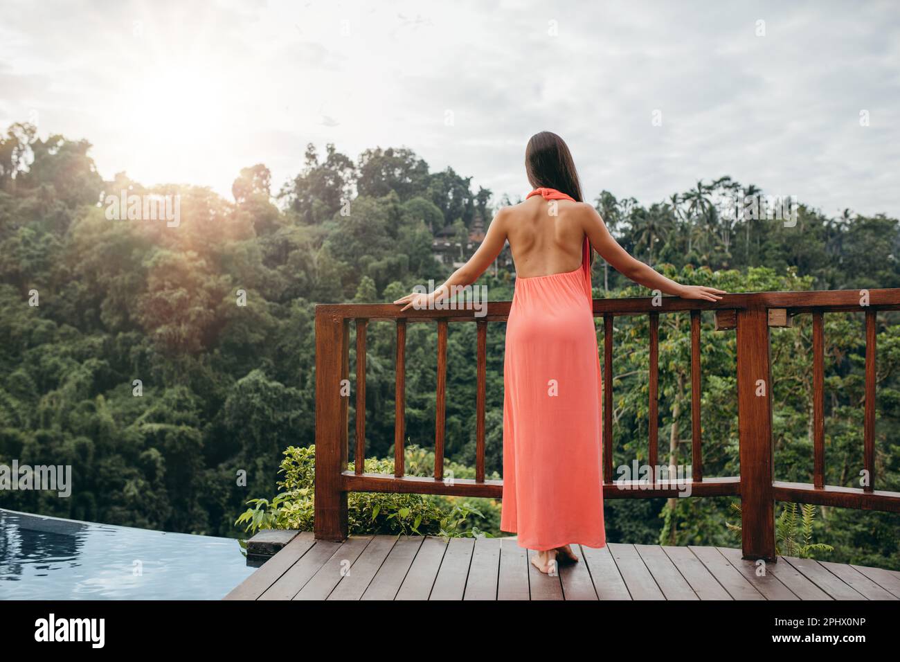 Ripresa della vista posteriore di una giovane donna in piedi accanto alla piscina e che guarda alla bella vista. Turista femminile in un resort di lusso. Foto Stock