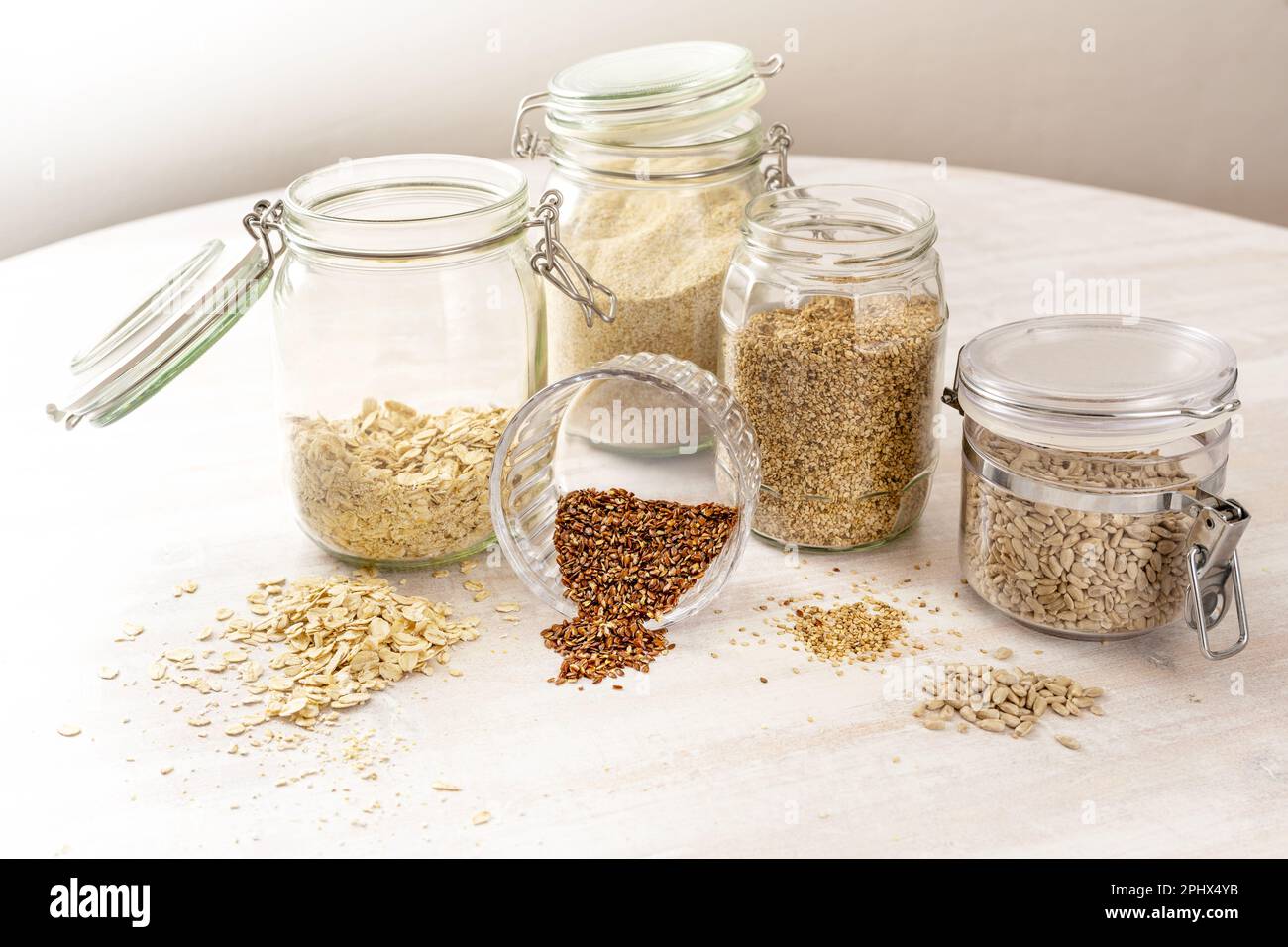 Cereali e semi come fiocchi di avena, semi di lino, semi di sesamo e girasole in vasi di vetro su un tavolo di legno chiaro, cibo sano, spazio copia, Foto Stock