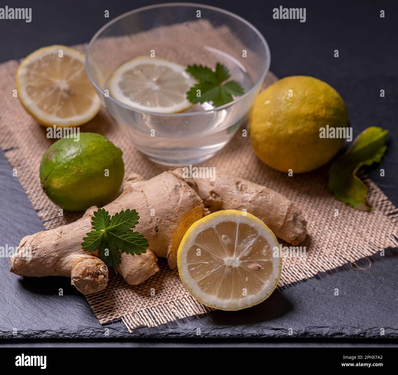 Composizione di zenzero e limone, con foglie verdi e un contenitore con fetta di limone in acqua Foto Stock