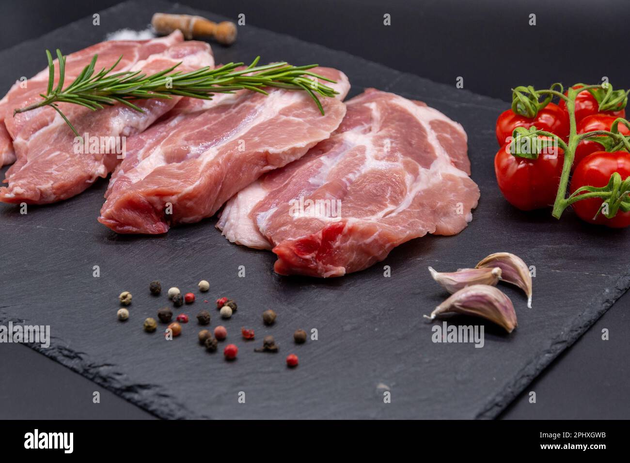 bistecca di maiale crudo e ingredienti su ardesia nera Foto Stock