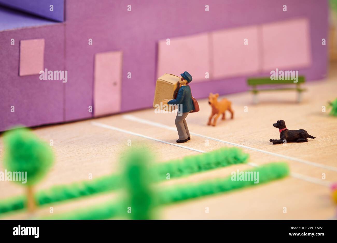 Vista laterale dall'alto del corriere giocattolo di plastica che trasporta la scatola di cartone al cliente in casa con i cani davanti Foto Stock